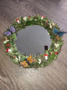 a wreath with butterflies on it sitting on top of a wooden floor next to a mirror