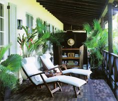 two lawn chairs sitting on top of a tiled floor next to plants and bookshelves