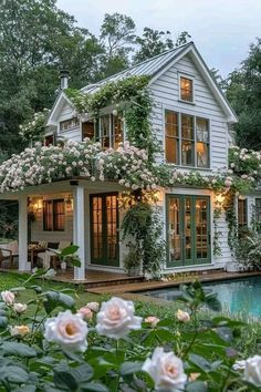 a white house with lots of windows and flowers on the roof, next to a pool