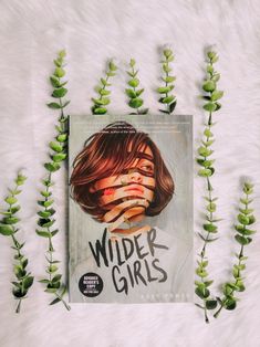 a book with the title wilder girls on it surrounded by green plant stems and leaves