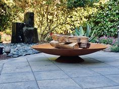 a wooden bowl sitting on top of a stone floor next to trees and bushes in the background