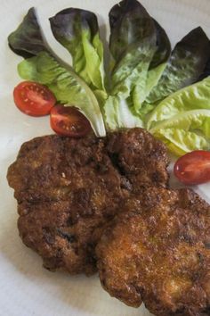 two fried meat patties with lettuce and tomatoes on a white paper plate