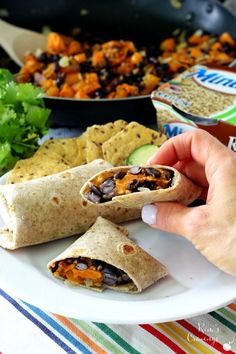 a person holding a burrito on a plate with other food items in the background