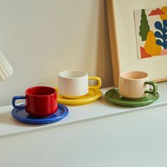 three cups and saucers are sitting on a shelf next to a framed art piece