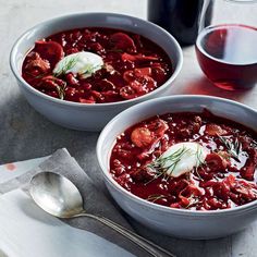 two bowls of chili with meat and sour cream on the side next to a glass of wine