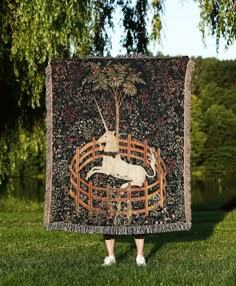 a person standing in the grass holding up a blanket with an image of a unicorn on it