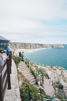 people are sitting at the edge of a cliff overlooking the ocean and beach with stairs leading up to them