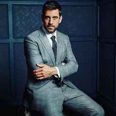 a man in a suit and tie sitting on a chair with his arms crossed looking at the camera