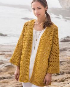 a woman standing on the beach wearing a yellow crocheted cardigan