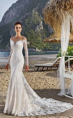 a woman standing on top of a sandy beach wearing a wedding dress with long sleeves