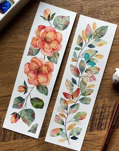 two watercolor bookmarks with flowers and leaves on them next to some paintbrushes