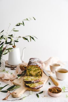 a loaf of bread sitting on top of a cutting board next to some cups and saucers