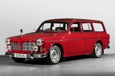 an old red station wagon is parked in a room with white walls and flooring