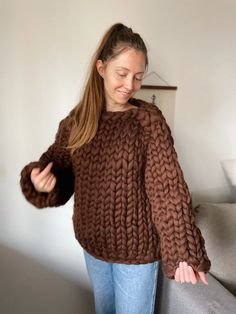 a woman wearing a brown sweater and jeans standing in front of a couch with her hands on her hips