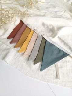 a bunch of different colored ties laying on top of a white cloth next to some dried flowers