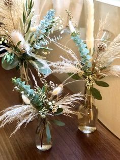 two vases with flowers and feathers on a table