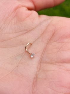 a person's hand holding a tiny diamond nose ring in their left hand, with grass in the background