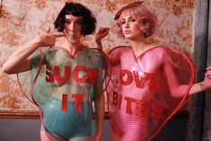 two women dressed in bodysuits with words on them