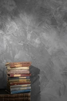 a stack of books sitting on top of a wooden table next to a gray wall