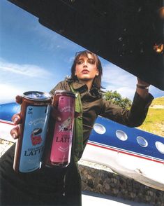 a woman holding two cans of wine in front of an airplane with the door open