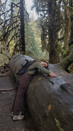 a man laying on top of a large log in the woods next to some trees