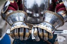 a close up of a person wearing armor and holding two metal gloves on their hands