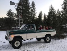 people are sitting in the bed of a green and white pick up truck on snow covered ground