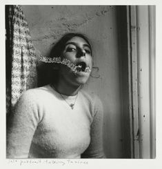 black and white photograph of a woman with fake teeth in front of a curtained window