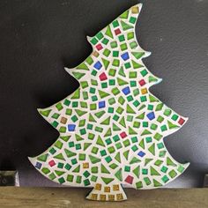 a ceramic christmas tree sitting on top of a wooden table next to a black wall