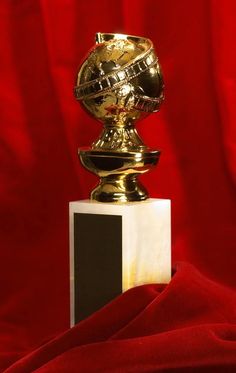 a golden trophy sitting on top of a white and black block in front of a red curtain