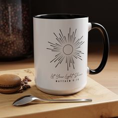 a white and black coffee mug sitting on top of a cutting board next to a spoon