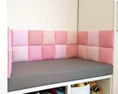 a pink and grey bench with lots of pillows on top of it in front of a white wall