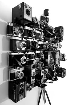 a bunch of old cameras are hanging on the wall next to a camera tripod