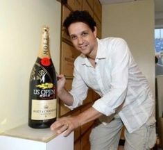 a man standing next to a bottle of wine on top of a white countertop