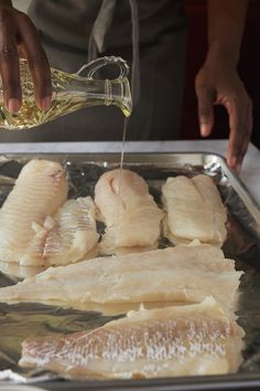 someone is pouring oil on some fish in a metal pan and another person is holding a glass bottle