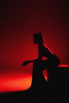 the silhouette of a woman sitting on a bench in front of a red light,