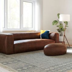 a living room with a brown leather couch and ottoman in front of a large window