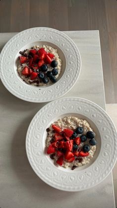 two white plates topped with oatmeal and berries on top of a table