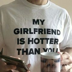 a person holding a cell phone and a cup with the words my girlfriend is hotter than you on it