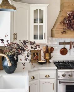 a kitchen with white cabinets and gold accents on the counter top, along with a vase filled with flowers