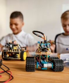 two children sitting at a table with remotes and toy cars in front of them