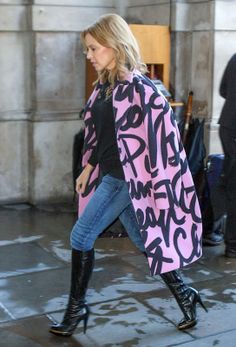 a woman walking down the street with a pink and black coat over her shoulders that has graffiti on it