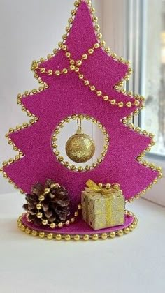 a pink christmas tree with gold ornaments and a present under the ornament is sitting on a window sill