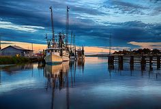 two boats are docked in the water at sunset or dawn with dark clouds above them