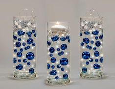 three glass vases with blue and white balls on them, one has a lit candle in the middle