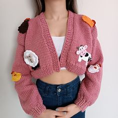 a close up of a doll wearing a pink cardigan with patches and flowers on it