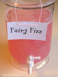 a glass jar filled with pink liquid sitting on top of a table next to a sign that says fairy fizz