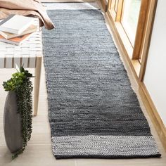 a long gray rug is on the floor next to a vase with plants in it