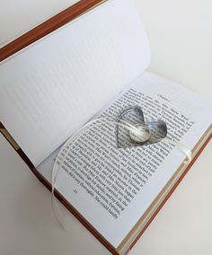 an open book with a heart shaped object on the page and string attached to it