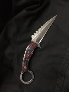 a knife that is sitting on top of a black cloth with red and white designs